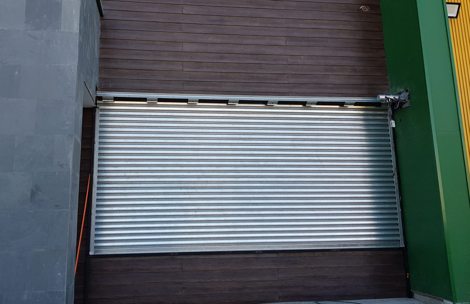 Cortina metálica emballetada galvanizada instalada en fachada de local comercial con revestimiento de madera